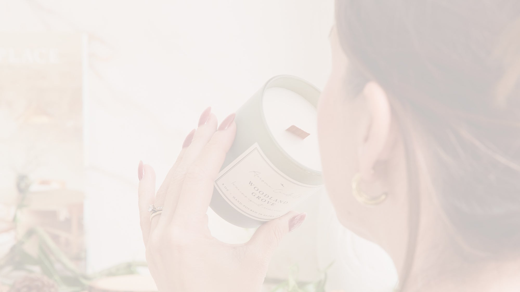 A faded image of a woman smelling the "Woodland Grove" candle.