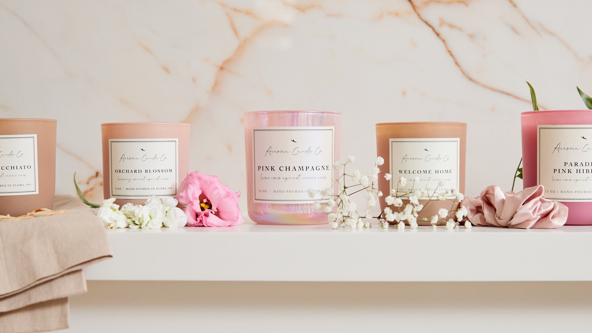 5 Aeroma Candles from the Spring collection sitting on a mantle with flowers around them