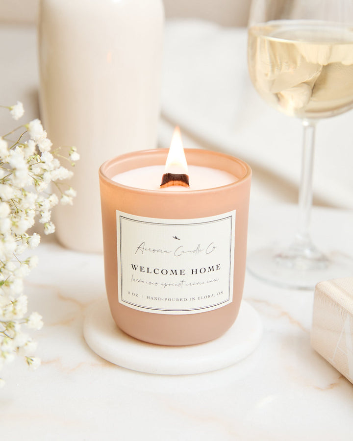 A khaki-colored glass candle on a white marble coaster, surrounded by white baby&