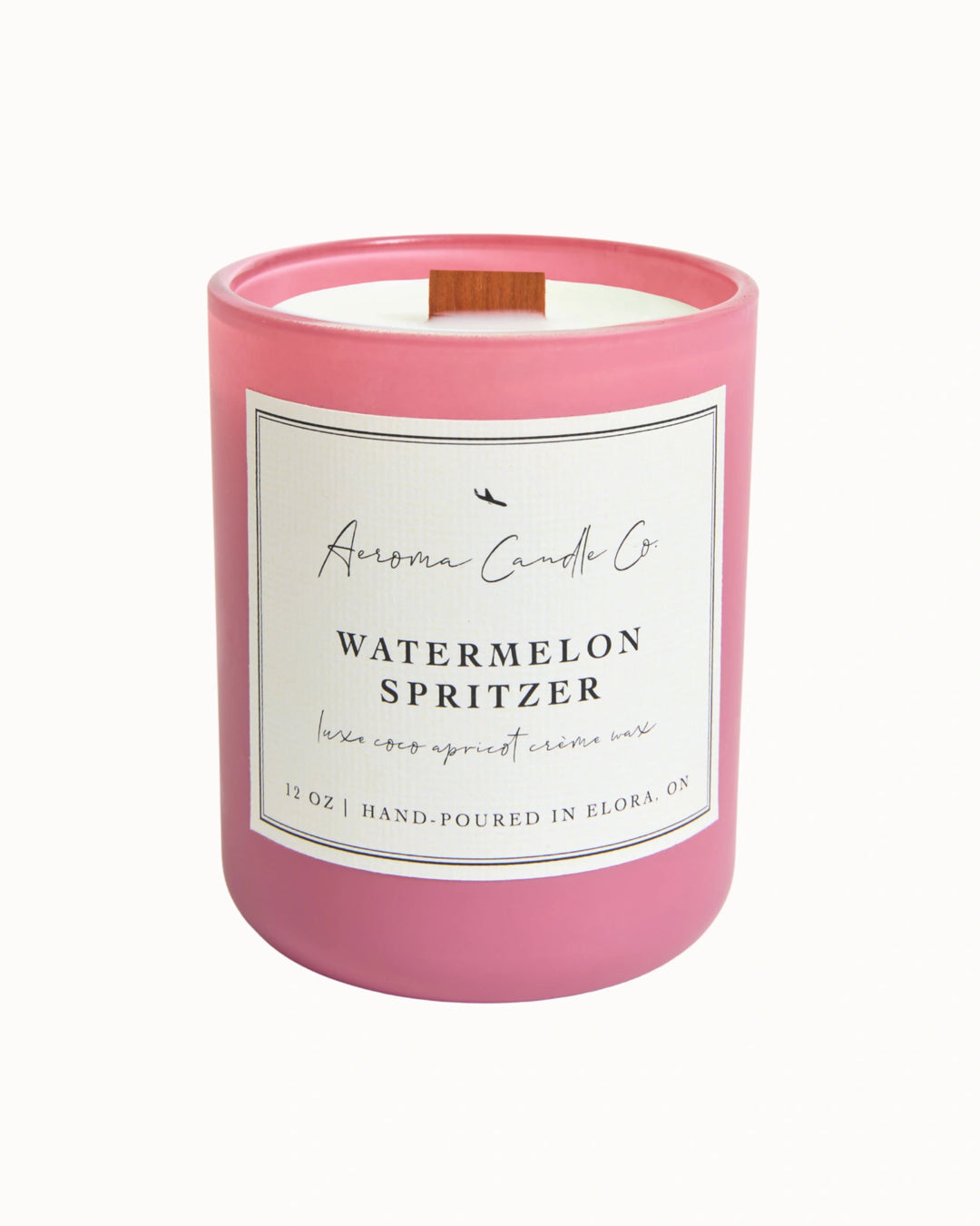 "Watermelon Spritzer" candle in a pink jar. There is a white square label on the candle stating the name of the business, scent, "luxe coco apricot crème wax", size, and "hand-poured in Elora, ON".