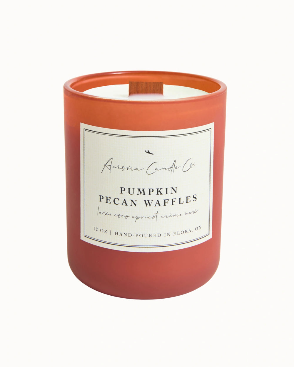"Pumpkin Pecan Waffles" candle in a dark orange jar. There is a white square label on the candle stating the name of the business, scent, "luxe coco apricot crème wax", size, and "hand-poured in Elora, ON".