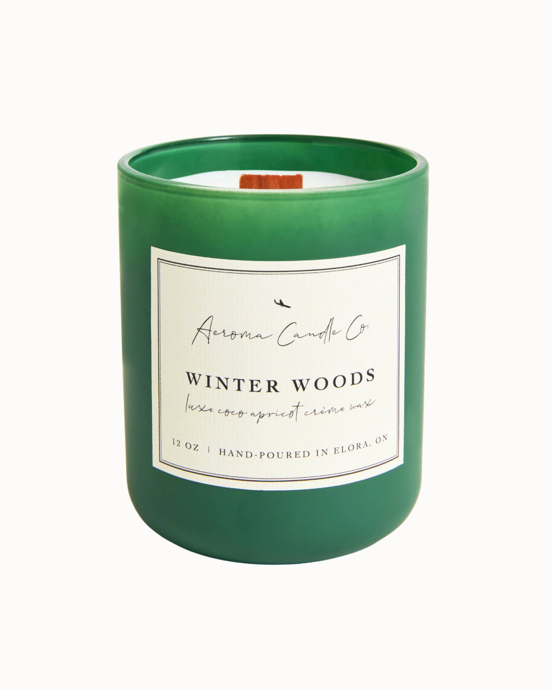 "Winter Woods" candle in a kelly green jar. There is a white square label on the candle stating the name of the business, scent, "luxe coco apricot crème wax", size, and "hand-poured in Elora, ON".