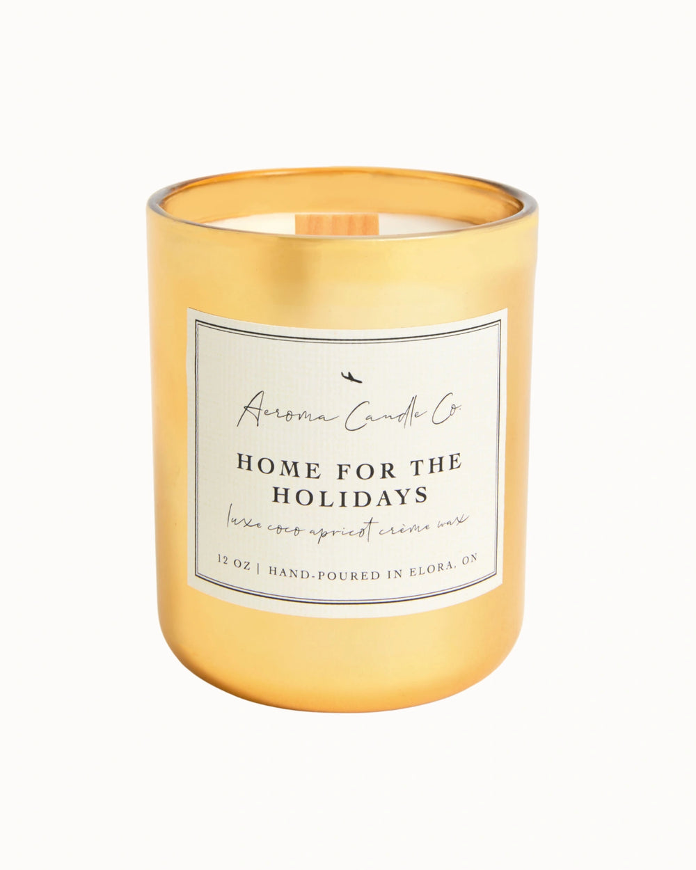 "Home For The Holidays" candle in a golden coloured jar. There is a white square label on the candle stating the name of the business, scent, "luxe coco apricot crème wax", size, and "hand-poured in Elora, ON".