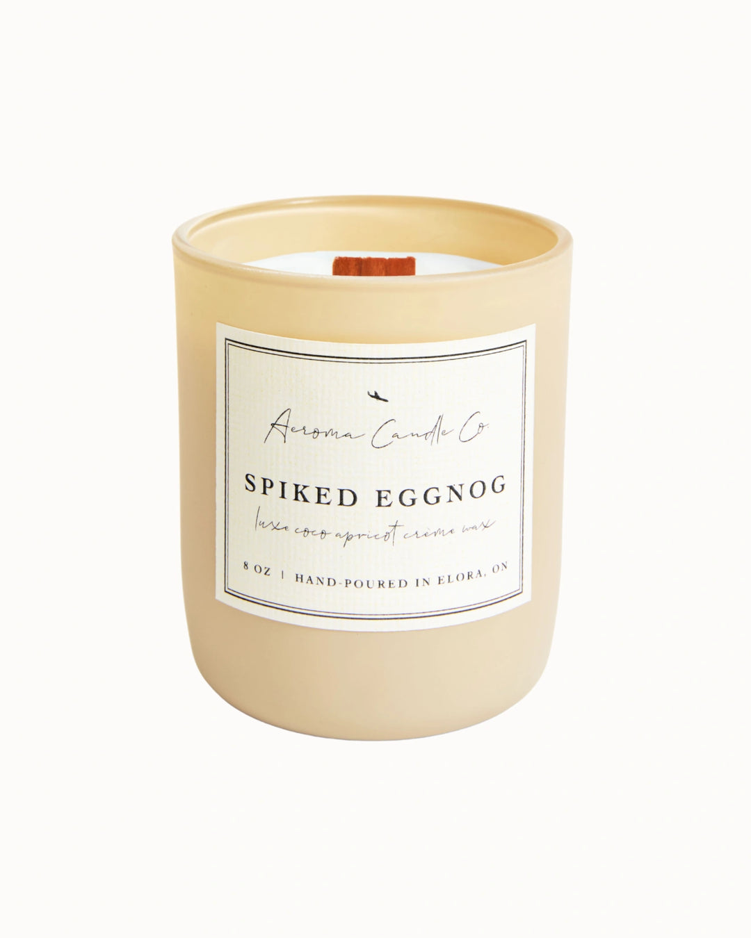"Spiked Eggnog" candle in a beige jar. There is a white square label on the candle stating the name of the business, scent, "luxe coco apricot crème wax", size, and "hand-poured in Elora, ON".