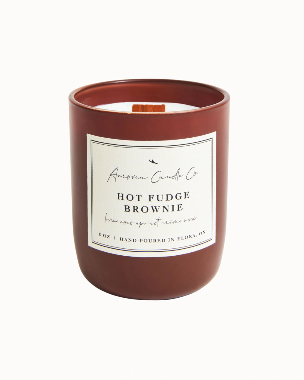 "Hot Fudge Brownie" candle in a dark brown jar. There is a white square label on the candle stating the name of the business, scent, "luxe coco apricot crème wax", size, and "hand-poured in Elora, ON".