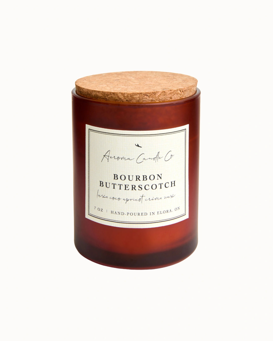 "Bourbon Butterscotch" candle in an opaque brown jar with a cork lid. There is a white square label on the candle stating the name of the business, scent, "luxe coco apricot crème wax", size, and "hand-poured in Elora, ON".