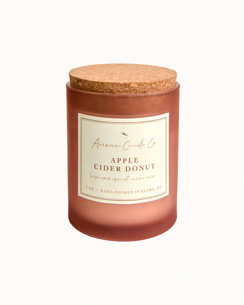 "Apple Cider Donut" candle in an opaque mahogany jar with a cork lid. There is a white square label on the candle stating the name of the business, scent, "luxe coco apricot crème wax", size, and "hand-poured in Elora, ON".