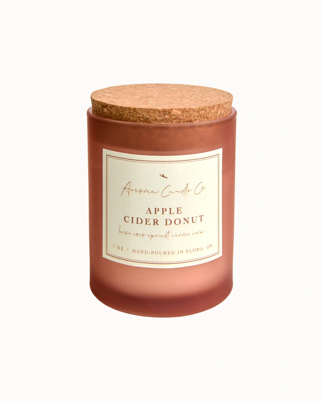 "Apple Cider Donut" candle in an opaque mahogany jar with a cork lid. There is a white square label on the candle stating the name of the business, scent, "luxe coco apricot crème wax", size, and "hand-poured in Elora, ON".