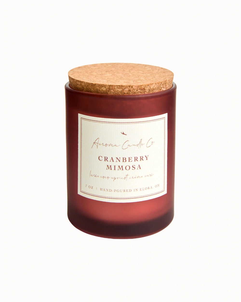 "Cranberry Minosa" candle in an opaque mahogany jar with a cork lid. There is a white square label on the candle stating the name of the business, scent, "luxe coco apricot crème wax", size, and "hand-poured in Elora, ON".