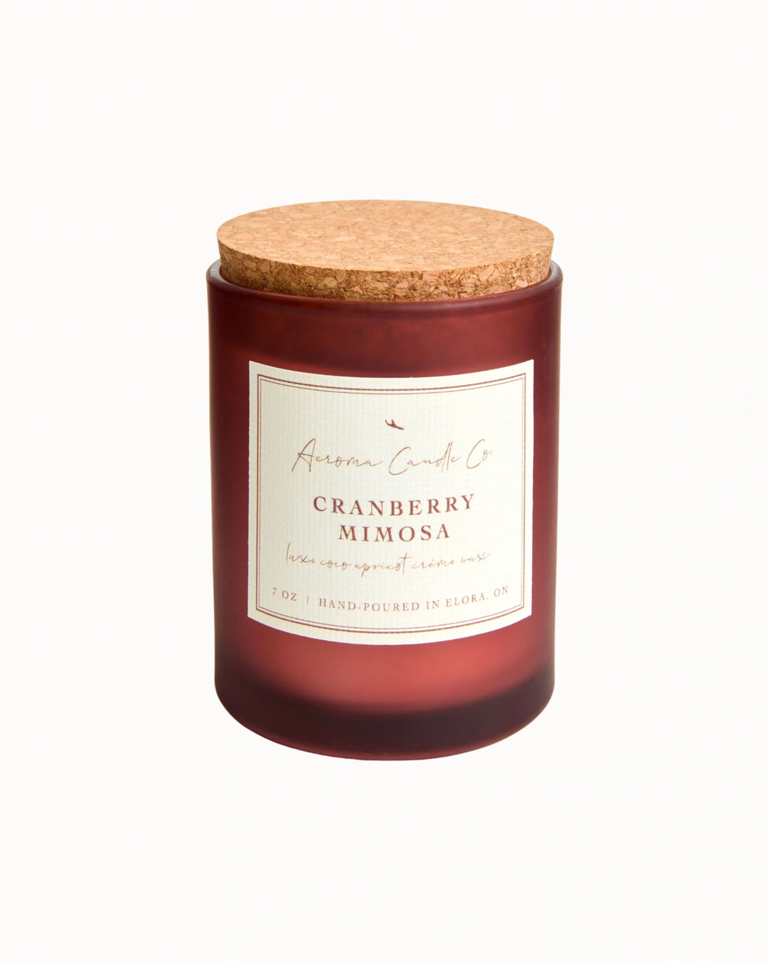 "Cranberry Minosa" candle in an opaque mahogany jar with a cork lid. There is a white square label on the candle stating the name of the business, scent, "luxe coco apricot crème wax", size, and "hand-poured in Elora, ON".