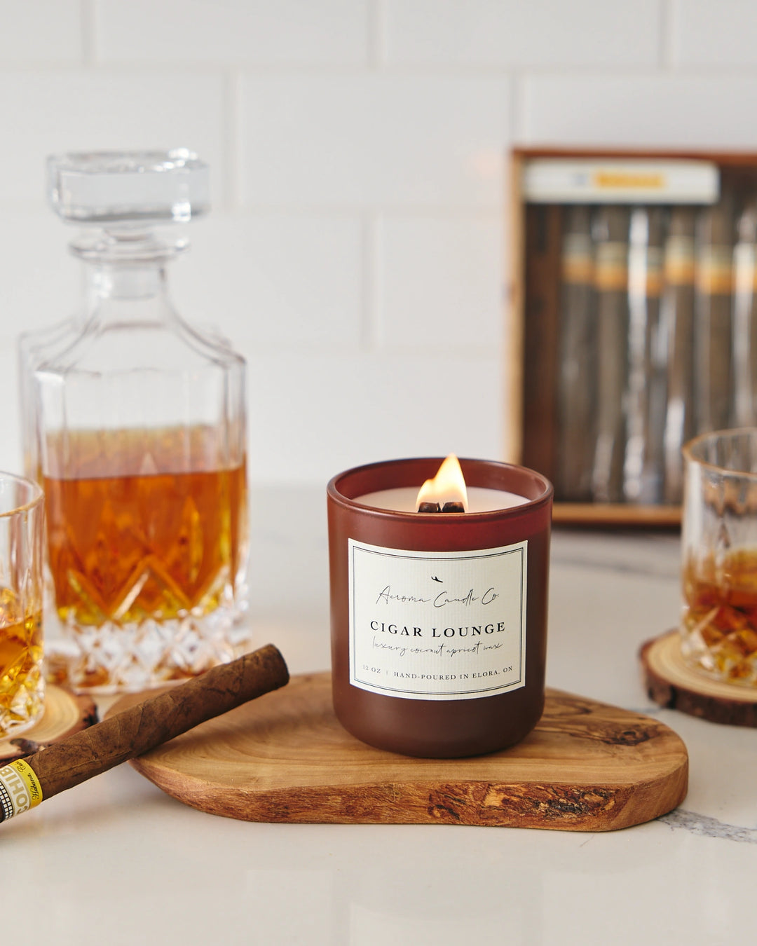 Candle labeled 'Cigar Lounge' with a decanter and glasses on a wooden coaster.
