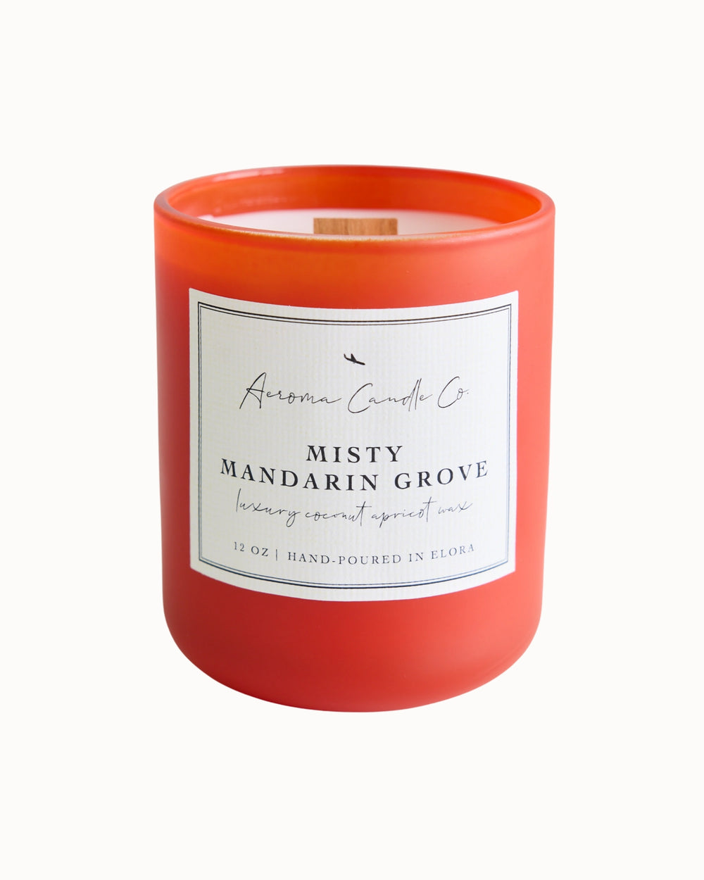 "Misty Mandarin Grove" candle in an orange jar. There is a white square label on the candle stating the name of the business, scent, "luxe coco apricot crème wax", size, and "hand-poured in Elora, ON".