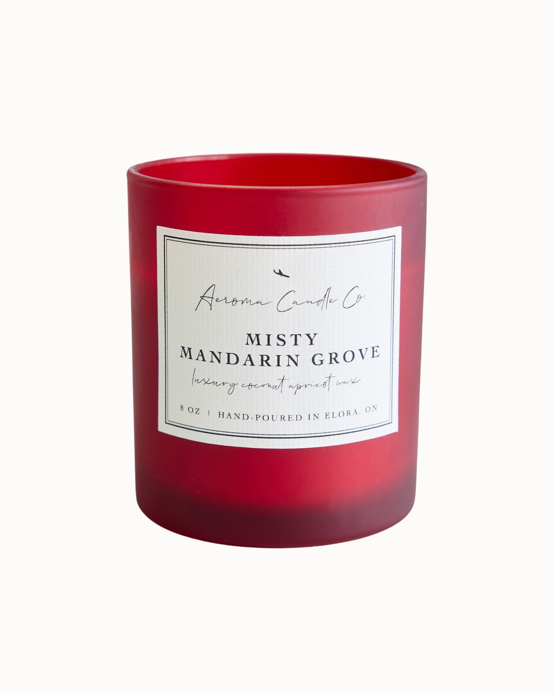 "Misty Mandarin Grove" candle in a translucent red jar. There is a white square label on the candle stating the name of the business, scent, "luxe coco apricot crème wax", size, and "hand-poured in Elora, ON".