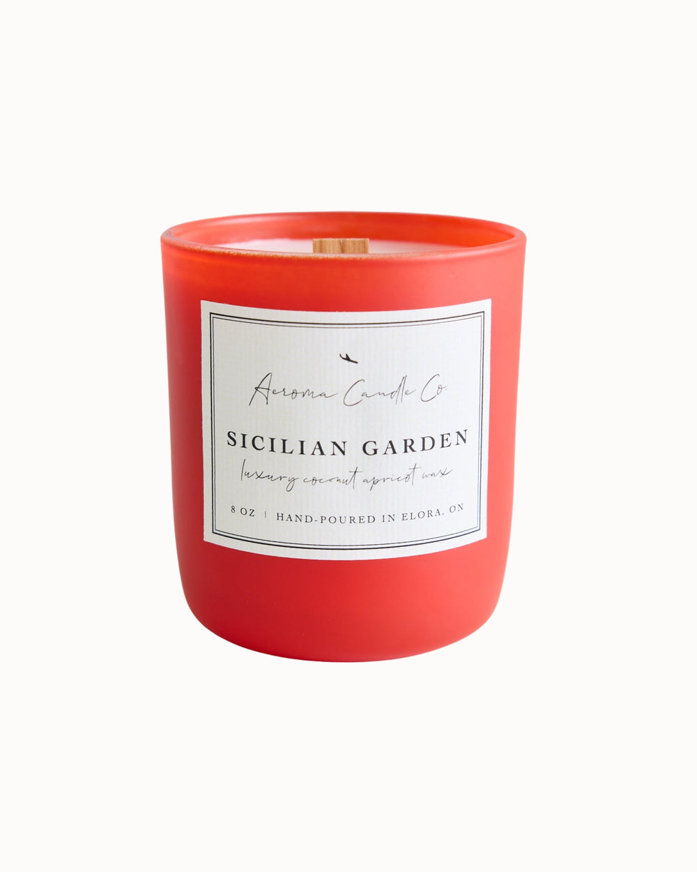 "Sicilian Garden" candle in an orangey red jar. There is a white square label on the candle stating the name of the business, scent, "luxe coco apricot crème wax", size, and "hand-poured in Elora, ON".