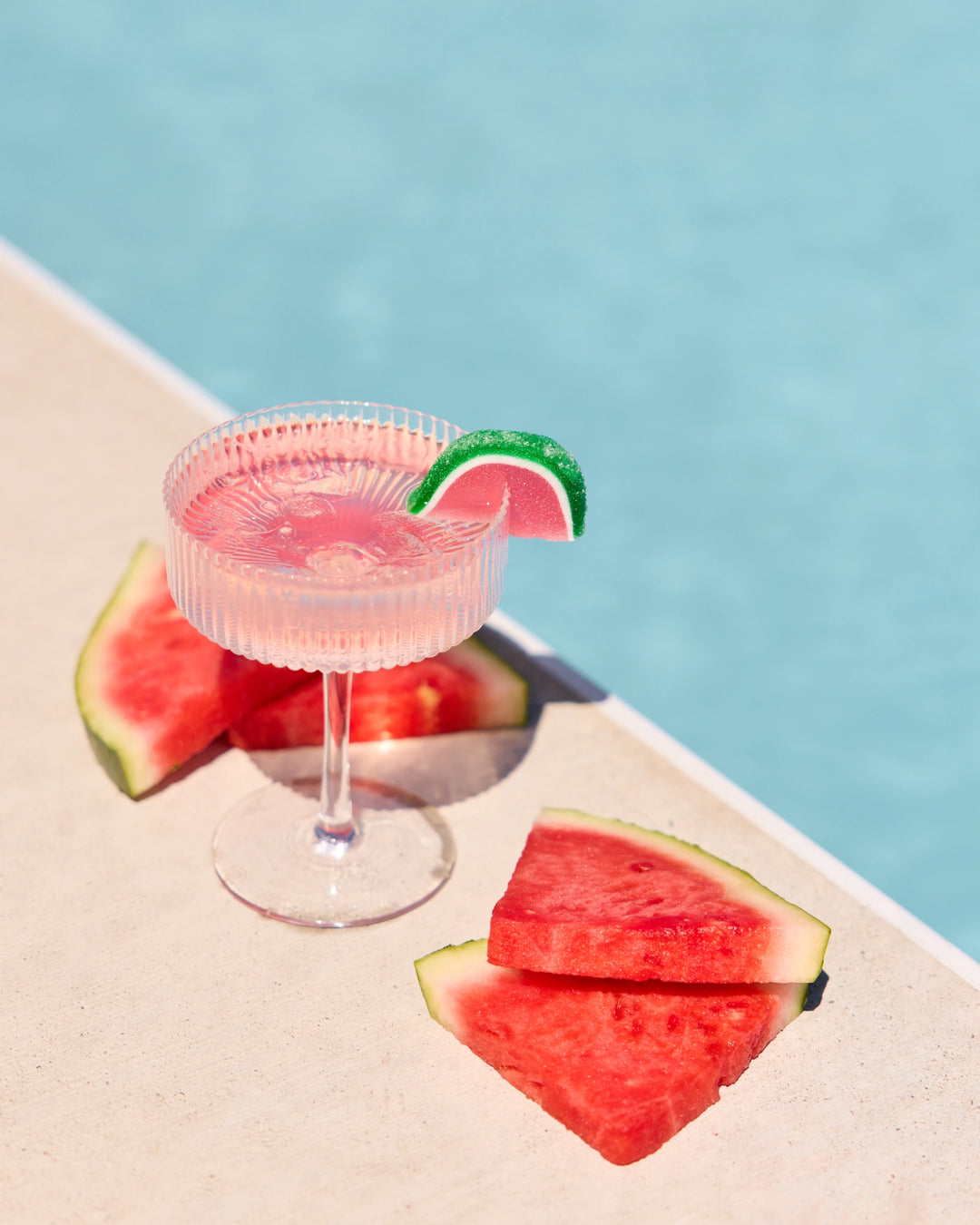 Pink cocktail in a glass with watermelon slices on a poolside setting