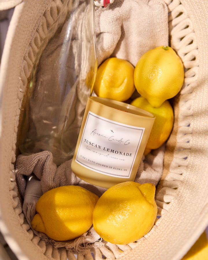 Candle labeled 'Tuscan Lemonade' surrounded by lemons in a woven basket.